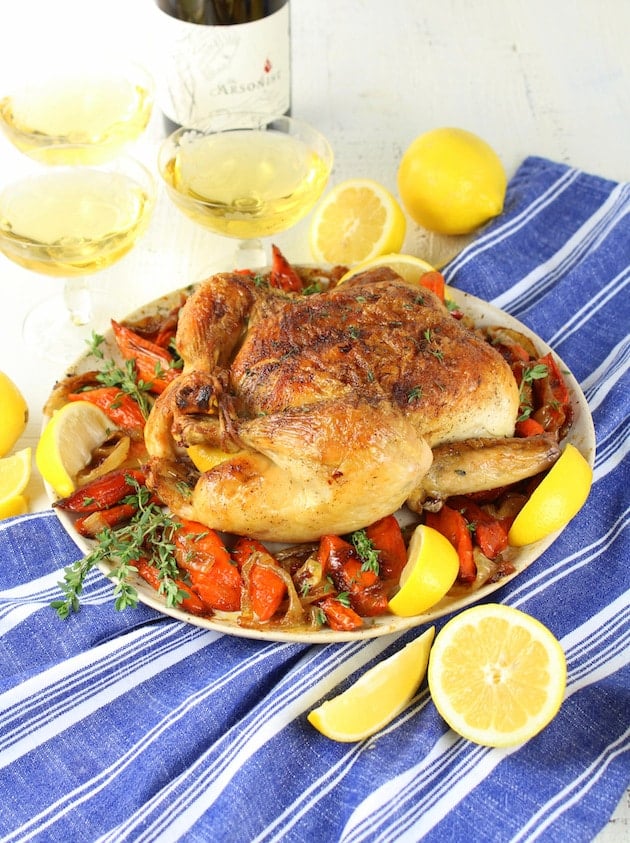 Cooked roast chicken on platter with wine glasses