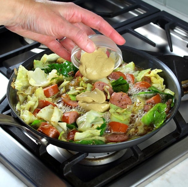 Adding dijon to pan of Kielbasa and Fried Cabbage