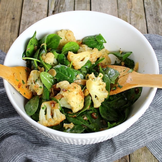 Warm Cauliflower Spinach Salad with wooden salad tongs on a farm table