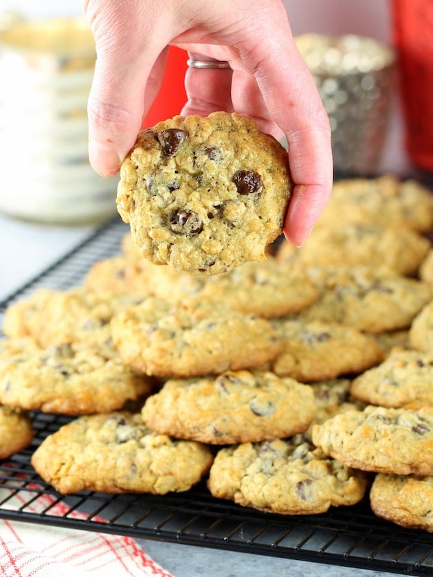 A person holding a cookie over a batch on a wire rack cooling.