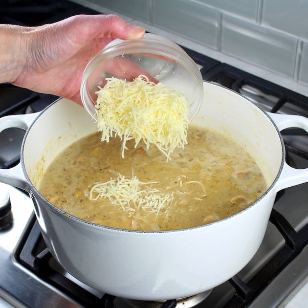 Adding cheese to chili in a large white pot