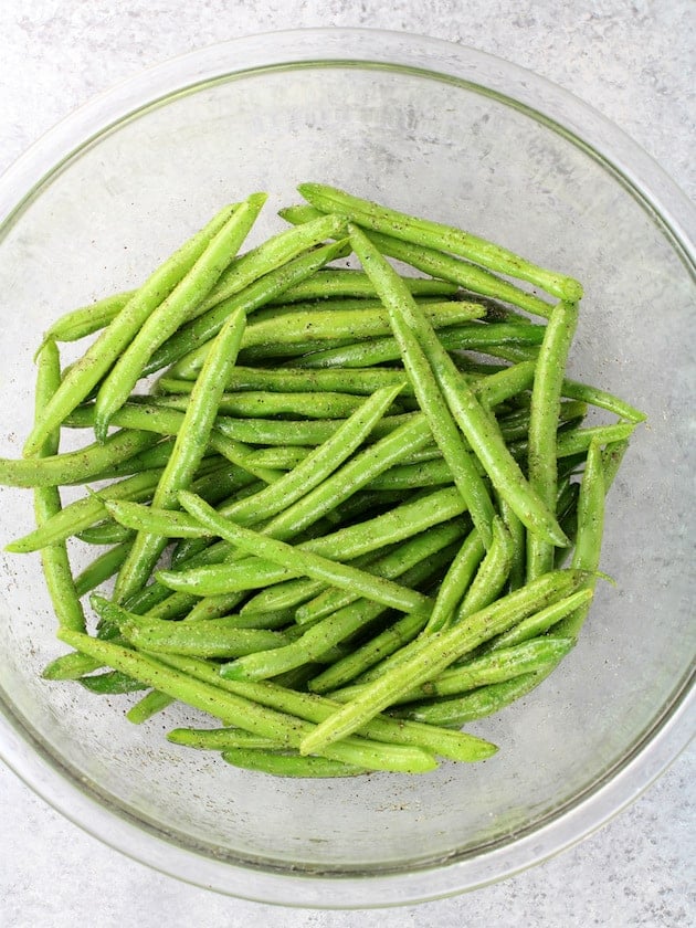 Raw Green Beans in large bowl with olive oil, salt and pepper.