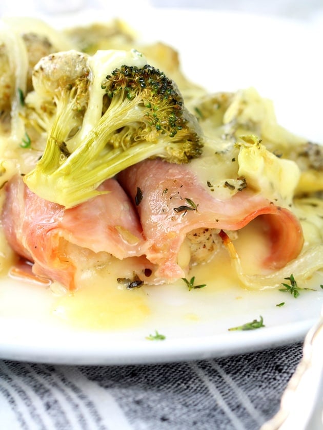 Close up plate with ham wrapped chicken and Swiss cheese and broccoli on top.