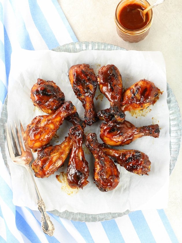 Grilled chicken legs on a platter with extra BBQ sauce on the side.