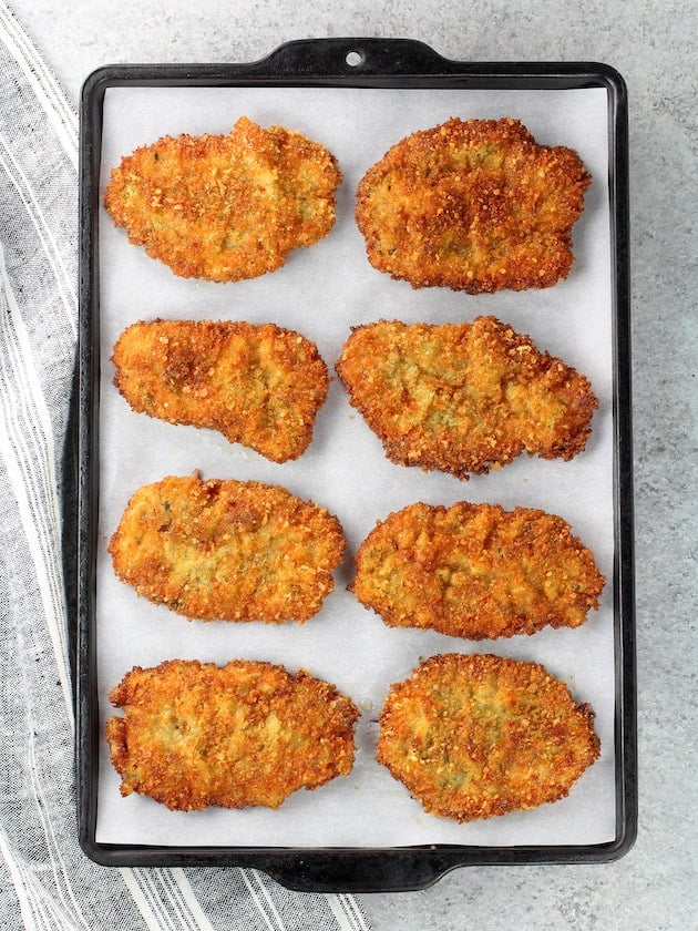 Eight breaded veal cutlets on a baking sheet