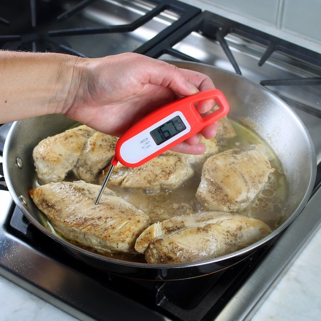using meat thermometer to check temperature of chicken breasts in skillet
