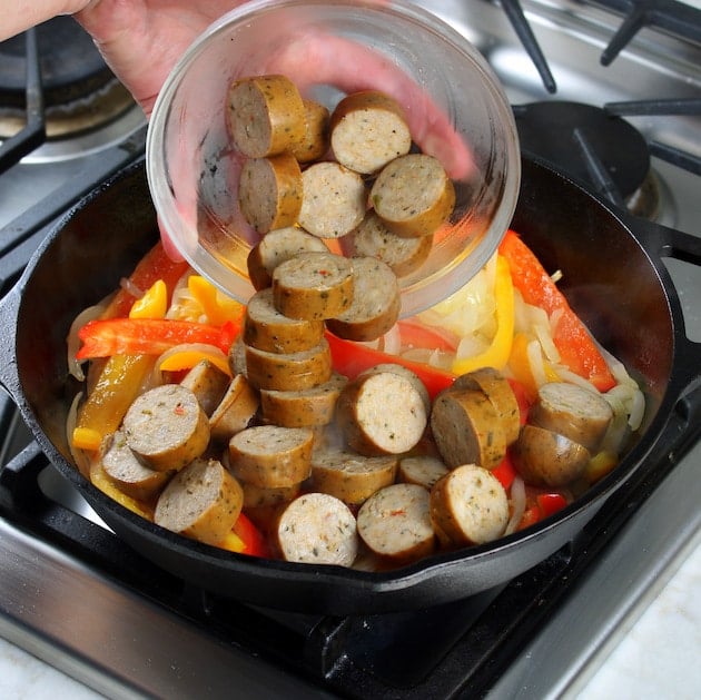 adding chicken sausage to skillet with bell peppers and onions