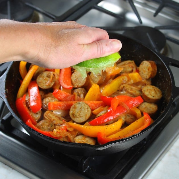 squeezing lime into a skillet of chicken sausage fajitas