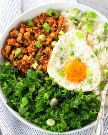 Fried egg in bowl with spicy Korean chicken meat, kale, and rice
