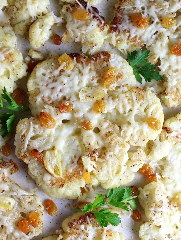 Roasted Cauliflower steaks with melted Asiago Cheese, Golden Raisins, and sliced garlic