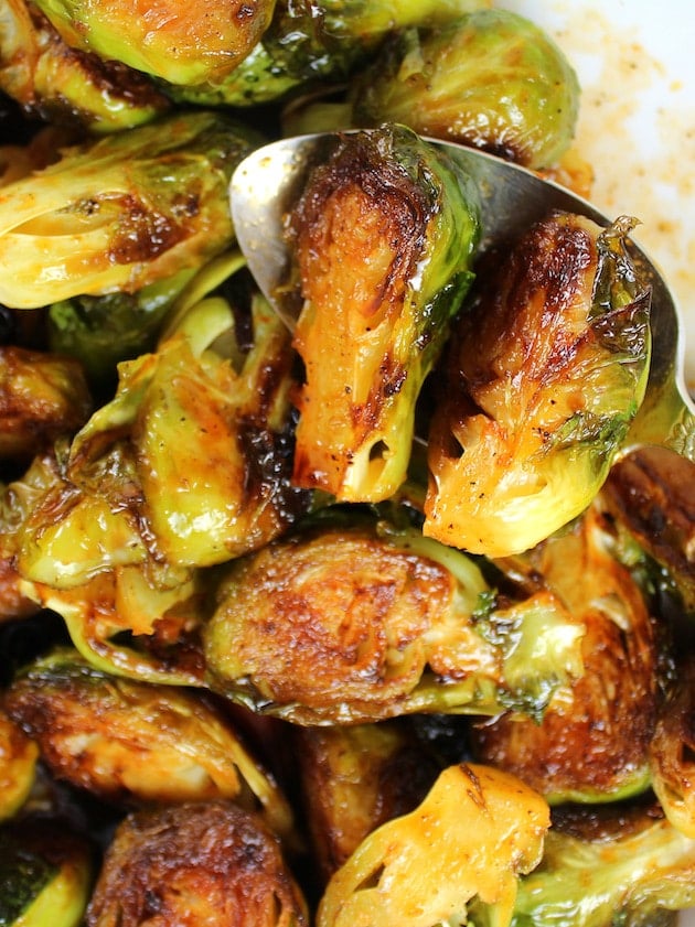 Spoon holding two cooked Brussels Sprouts over a serving bowl