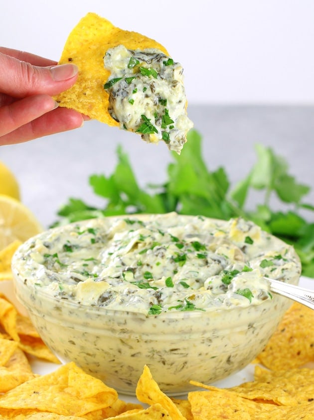 Hand holding corn chip with artichoke dip