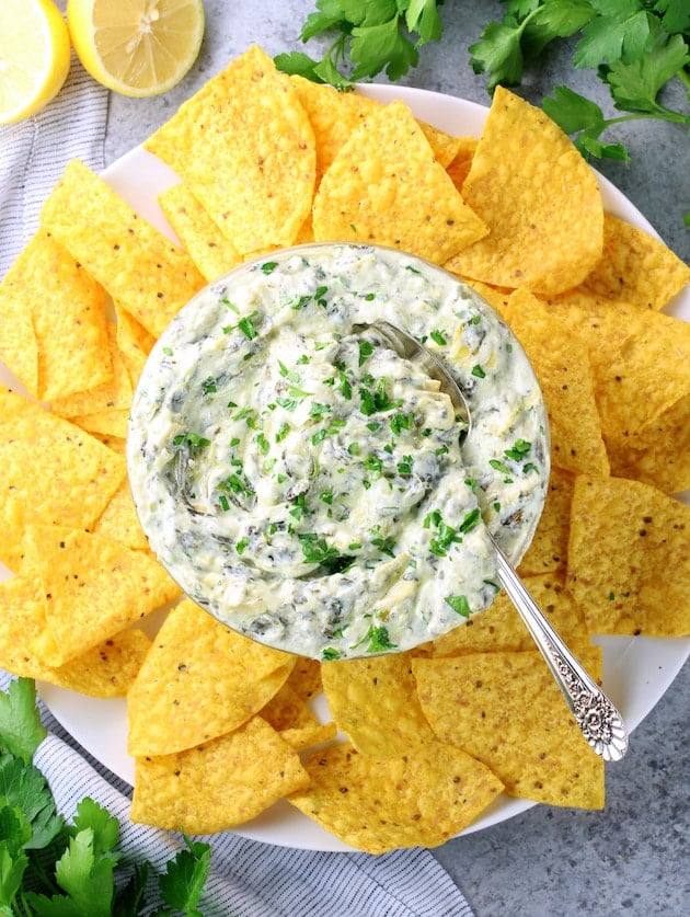 Bowl of spinach artichoke dip on plate full of corn chips.