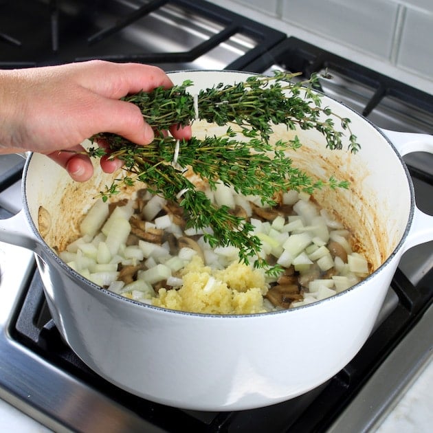 Adding bundles of herbs to large dutch oven for soup