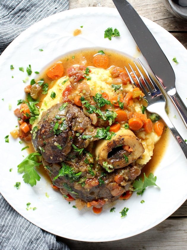 Cooked Veal Osso Buco veal shank on parmesan polenta with cooked carrots and gravy.