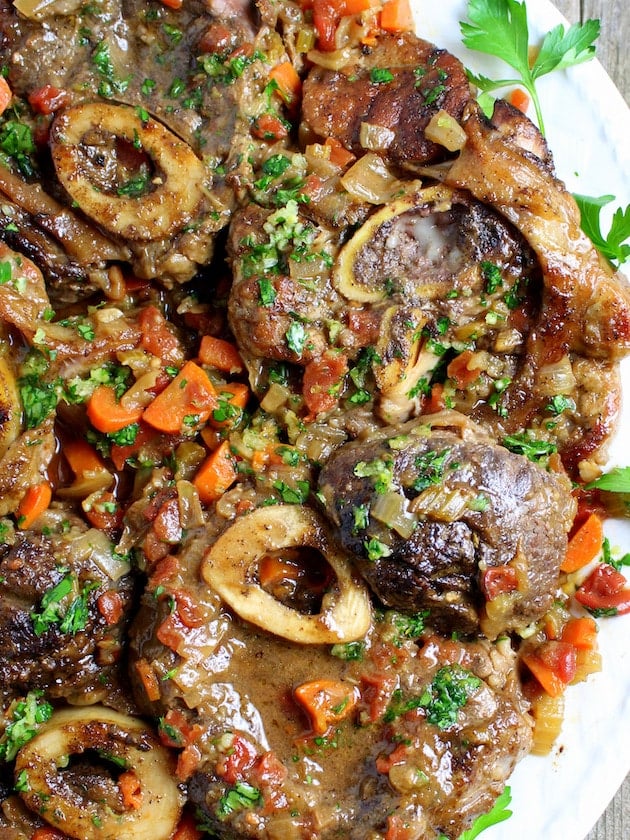 Slow roasted veal shanks on a plate with tomato and carrots.