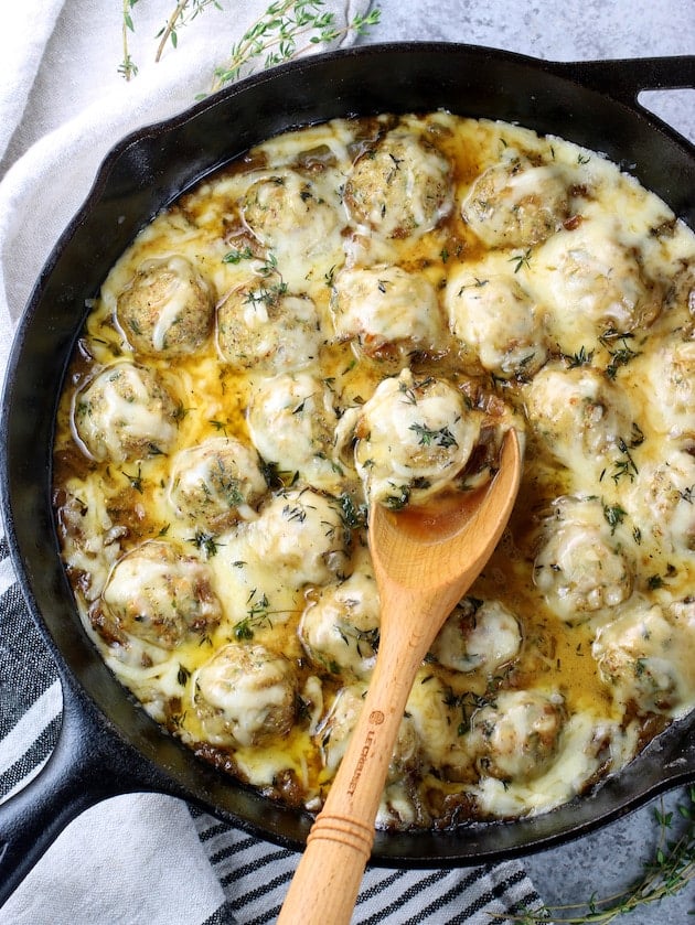 Skillet with cheesy meatballs and wooden sppon