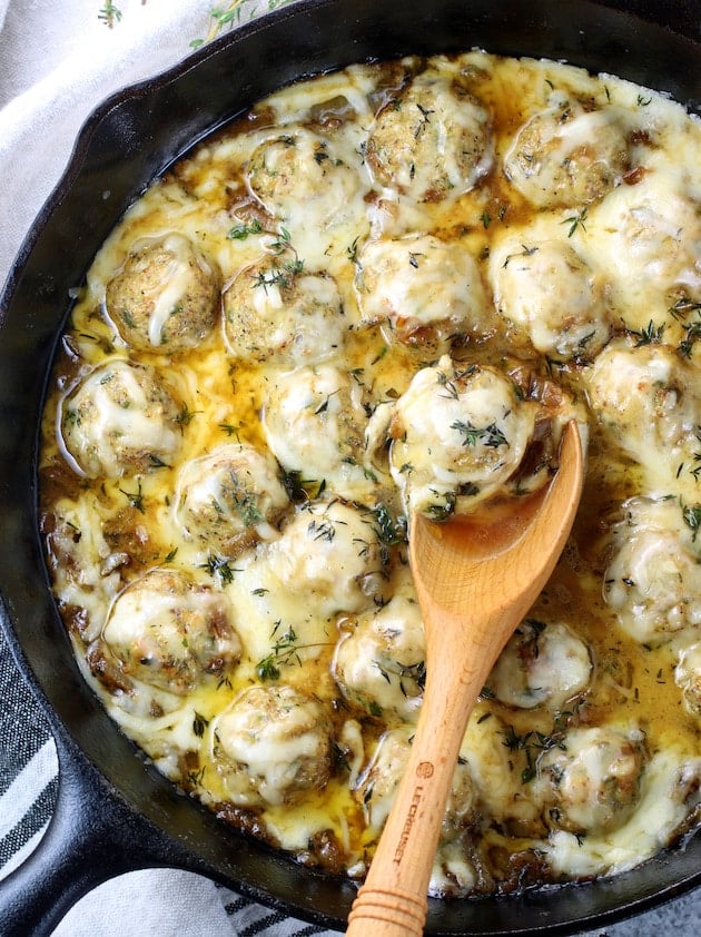 Meatballs smothered in melted cheese in a cast iron skillet