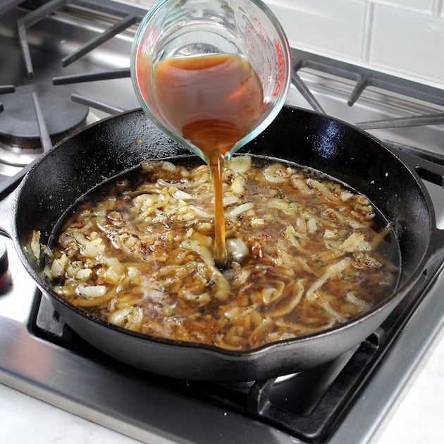 Adding beef stock to onions cooking on stovetop