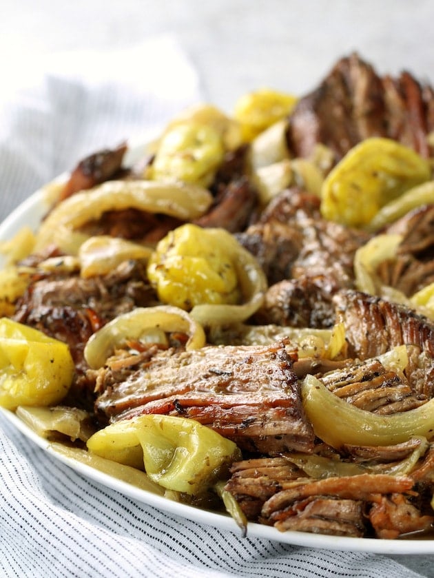 Eye level platter of pulled slow cooker Italian beef with onions and pepperoncini