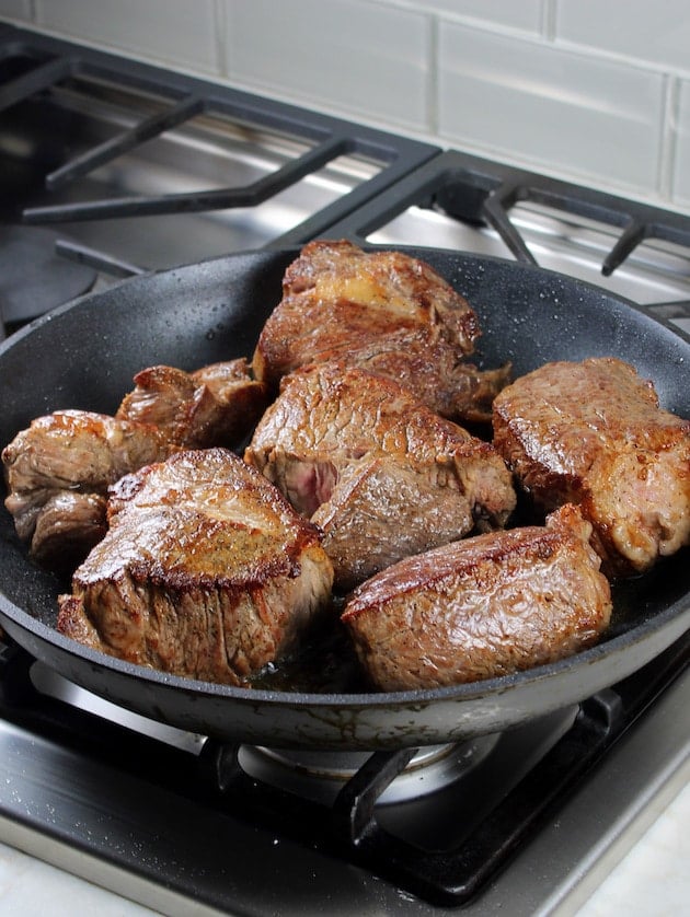 Beef cooking on a stove top oven in a saute pan