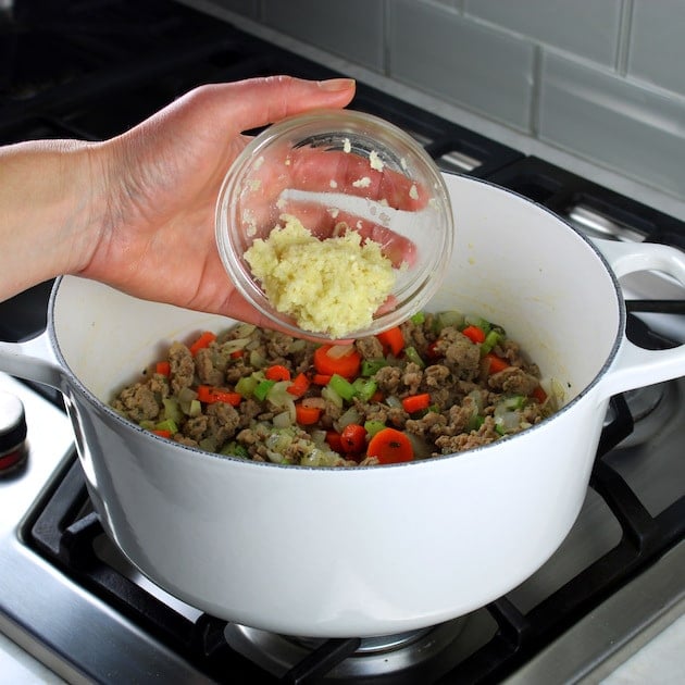 Adding garlic to large pot of pasta e fagioli soup