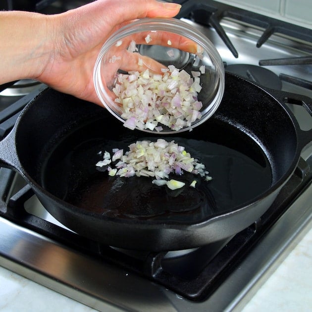 Adding shallots to a saute pan.