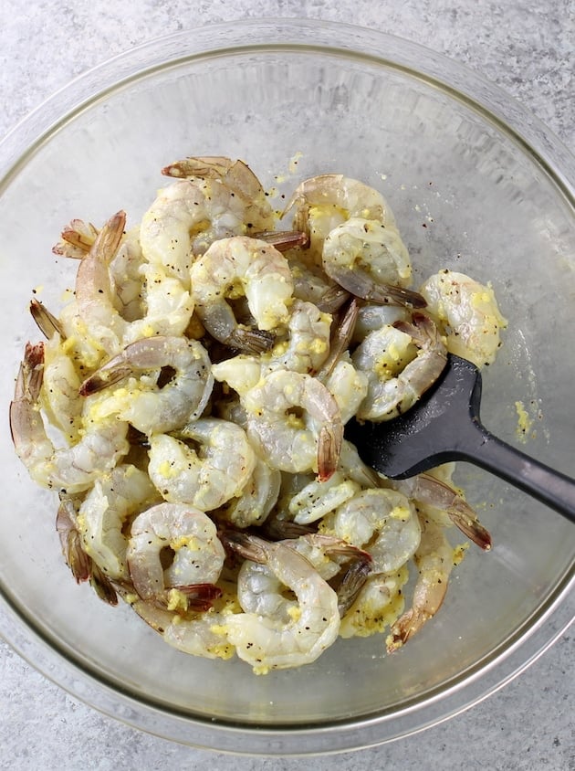 Shrimp tossed in marinade in a glass bowl