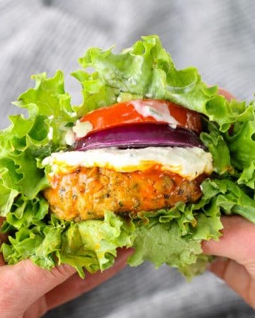 A close up of buffalo chicken burger with tomato and onion in a lettuce wrap