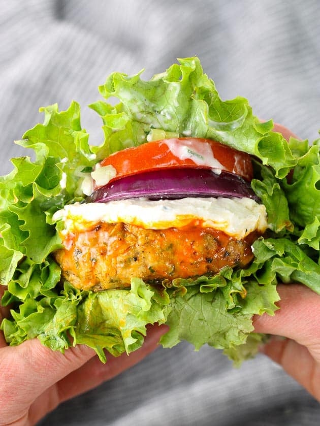 A close up of buffalo chicken burger with tomato and onion in a lettuce wrap