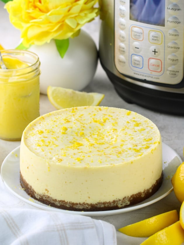 Whole instant pot lemon cheesecake with lemon zest, in front of instant pot