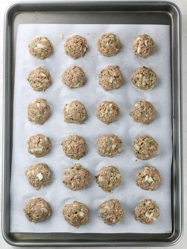 Two dozen meatballs on cookie sheet, ready to bake