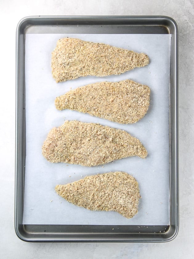 Breaded chicken cutlets on baking sheet ready to cook. 