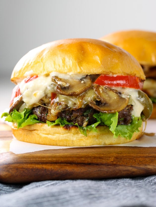 A close up of a cheeseburger with peppers and onions on a wooden cutting board