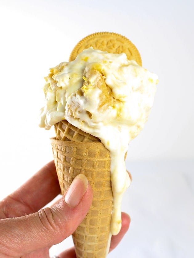 Close up hand holding a sugar cone with lemon ice cream dripping down