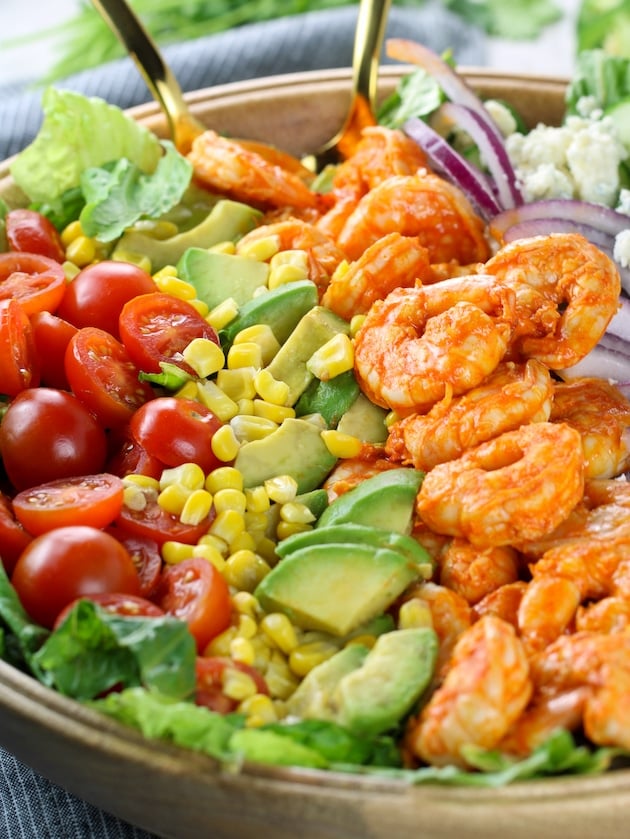 Partial dish eye level buffalo shrimp salad with gold serving utensils