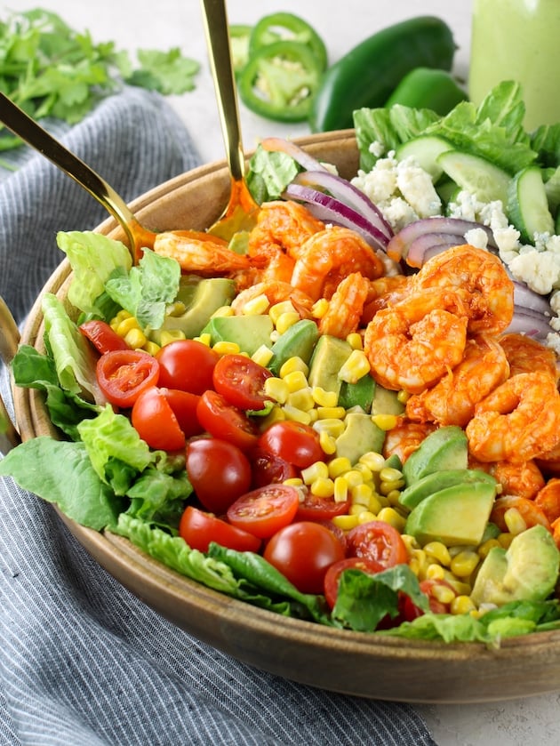 Partial bowl eye level shrimp in large salad with tomatoes, avocados, corn, red onions, and blue cheese