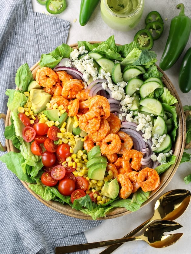 Fresh veggie buffalo shrimp salad in large wooden serving bowl with jalapenos and mason jar of dressing