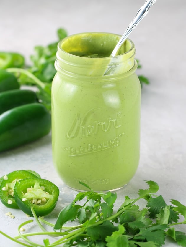 Mason jar with green avocado dressing and jalapenos in background