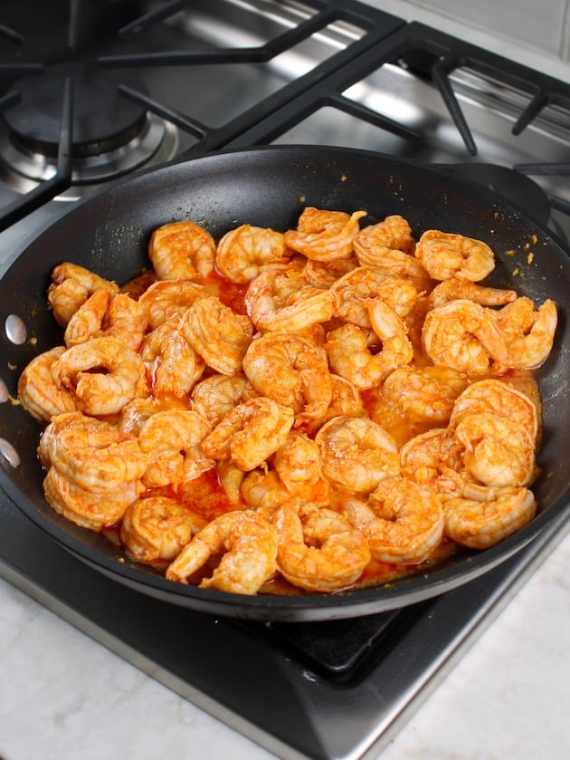 Saute pan full of buffalo shrimp cooking on stovetop