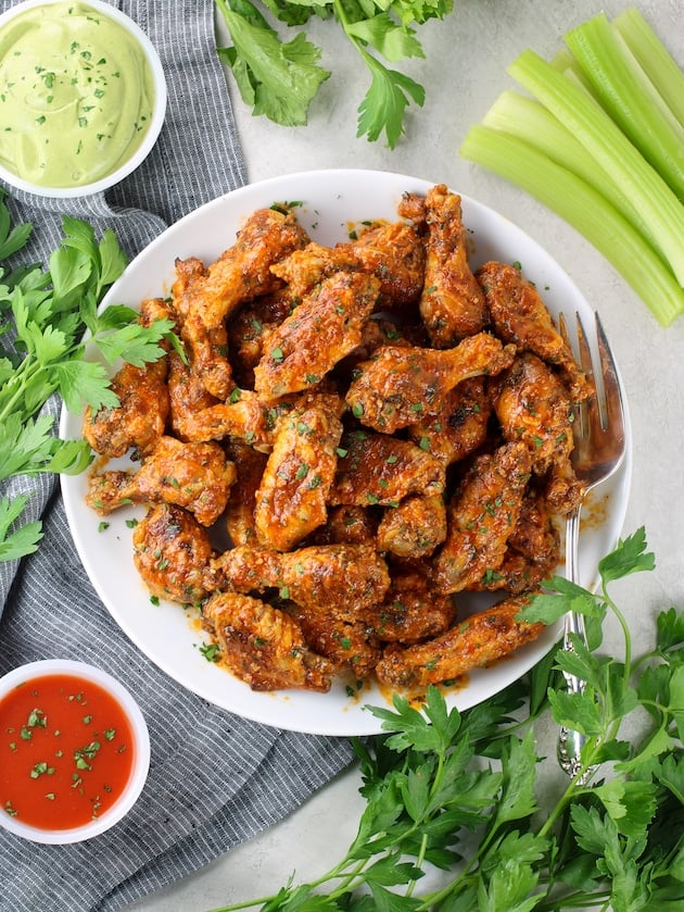Plate full of buffalo wings with celery, parsley, ranch dipping sauce and buffalo sauce