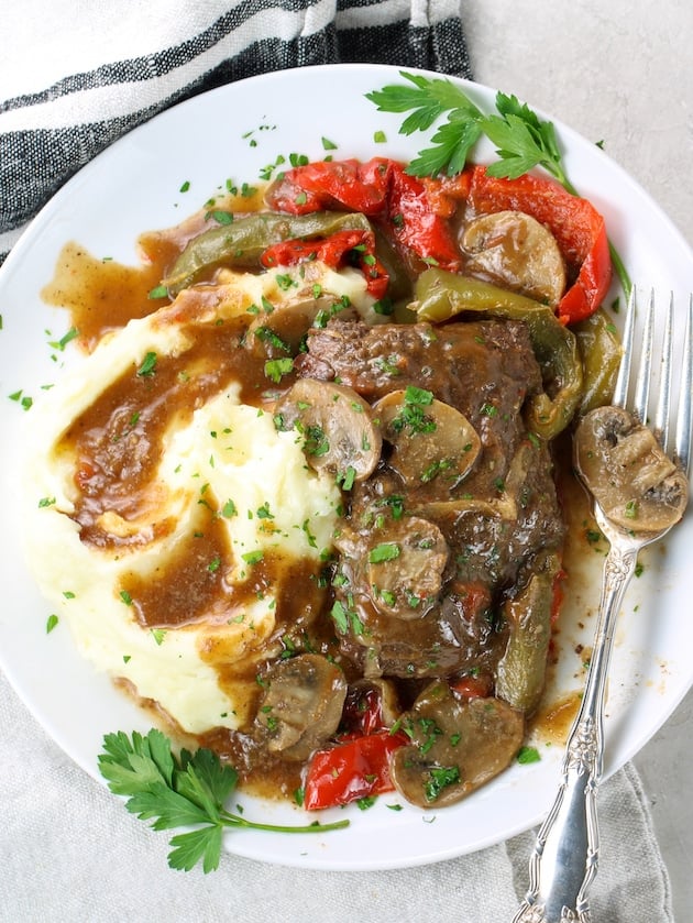 Plate with mashed potatoes, steak covered in mushrooms, peppers, and brown gravy