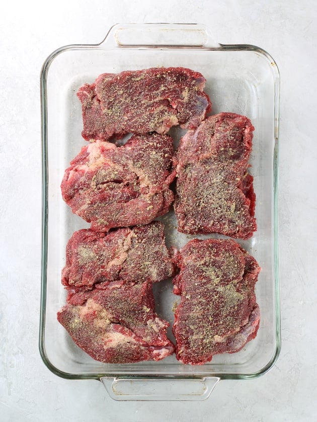 Chuck steak with seasonings in a glass casserole dish before cooking