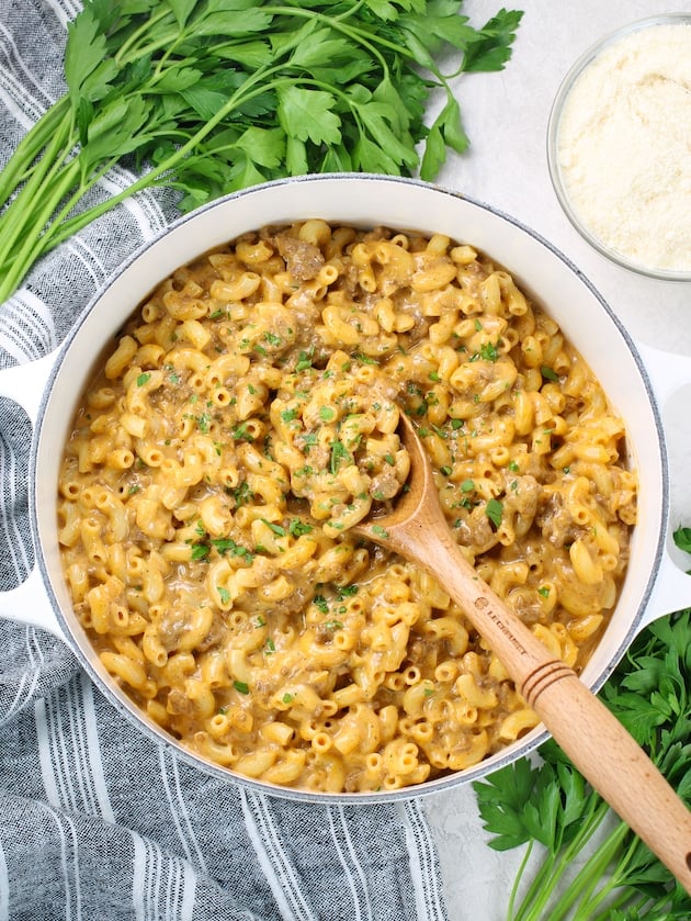 Pot full of macaroni and cheese with ground beef on a table with fresh parsley