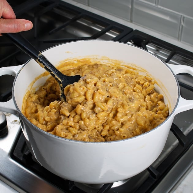 Stirring cooked macaroni elbow pasta into large pot with cheesy meat mixture