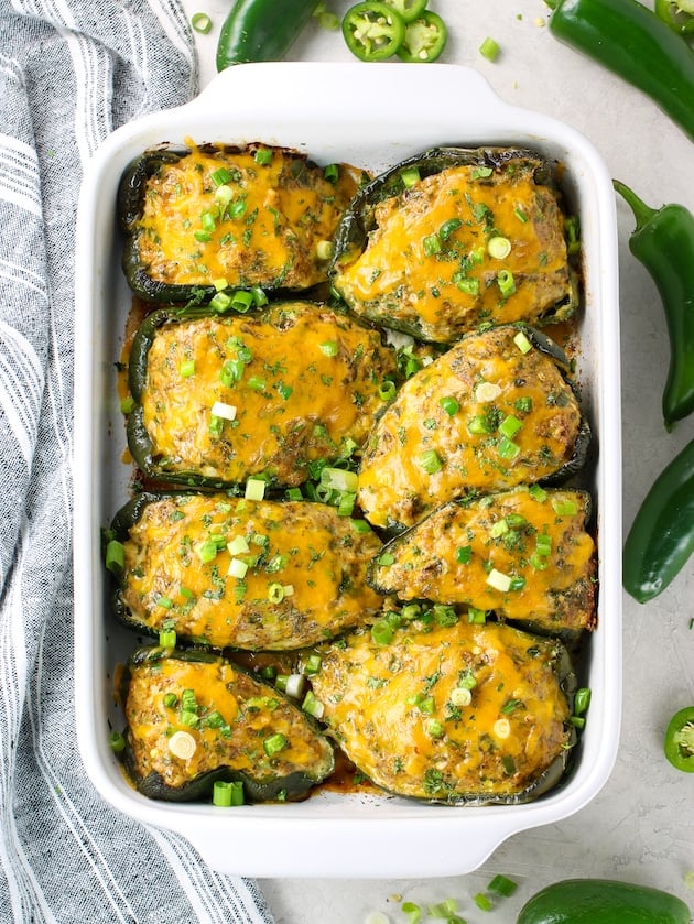 Casserole dish of baked stuffed peppers surrounded by fresh jalapenos 