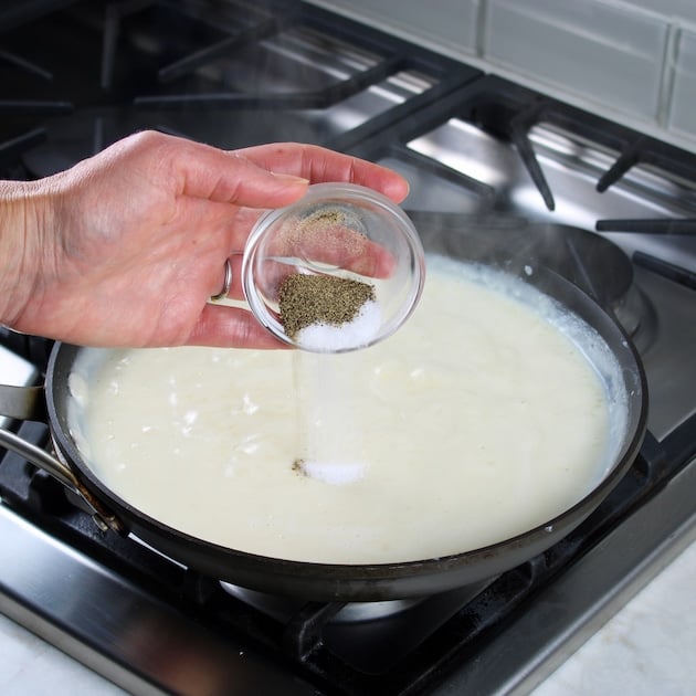 adding salt and pepper to cheesy sauce in a skillet on the stove