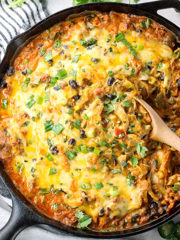 Wooden spoon scooping Cheesy Enchilada Dip out of cast iron skillet