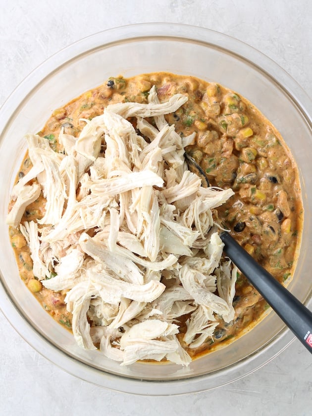 Adding shredded chicken to large glass bowl with the other ingredients.