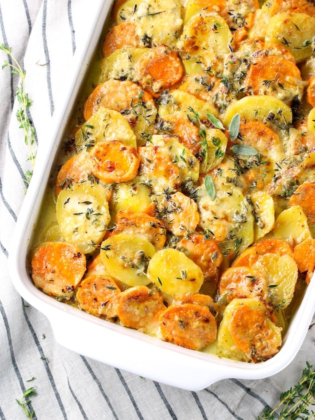 Casserole dish full of sliced yukon gold and sweet potatoes topped with gruyere cheese